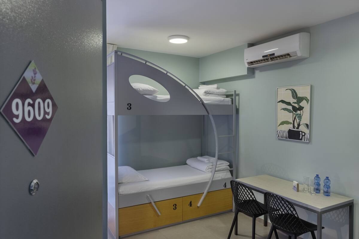 A bunk bed with a desk and chairs, an air conditioner, and a wall-mounted sign.