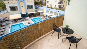 A balcony with a view of a swimming pool and outdoor seating area. - Almog Eilat (Eilat)