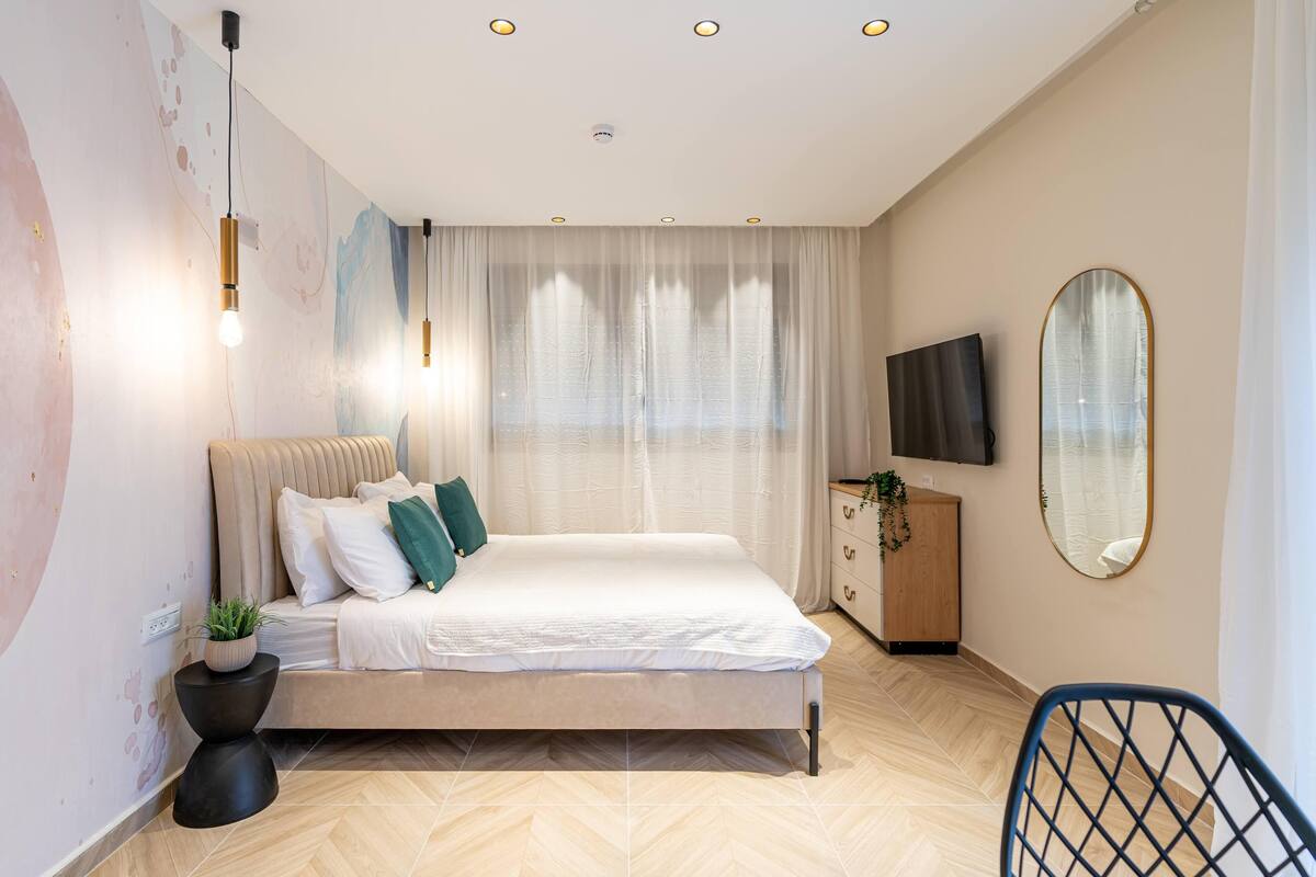 A modern bedroom with a bed, bedside tables, a TV, and a mirror.