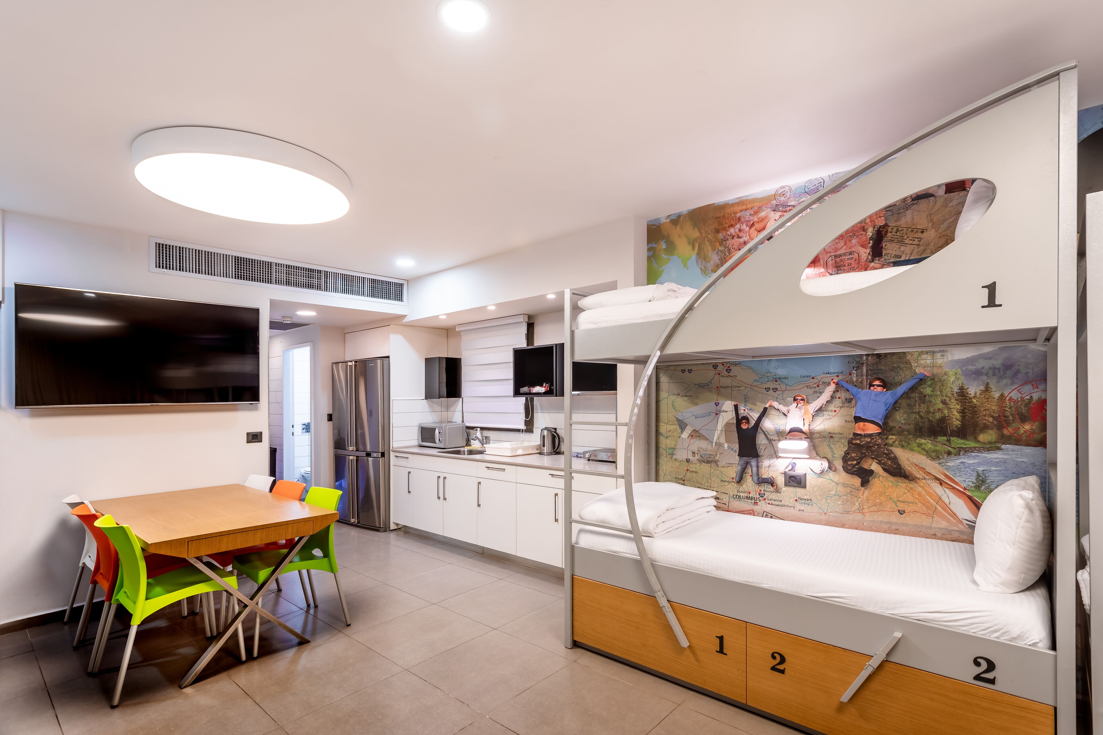 A bunk bed with a map mural, a dining area with a wooden table and colorful chairs, and a kitchenette with modern appliances.