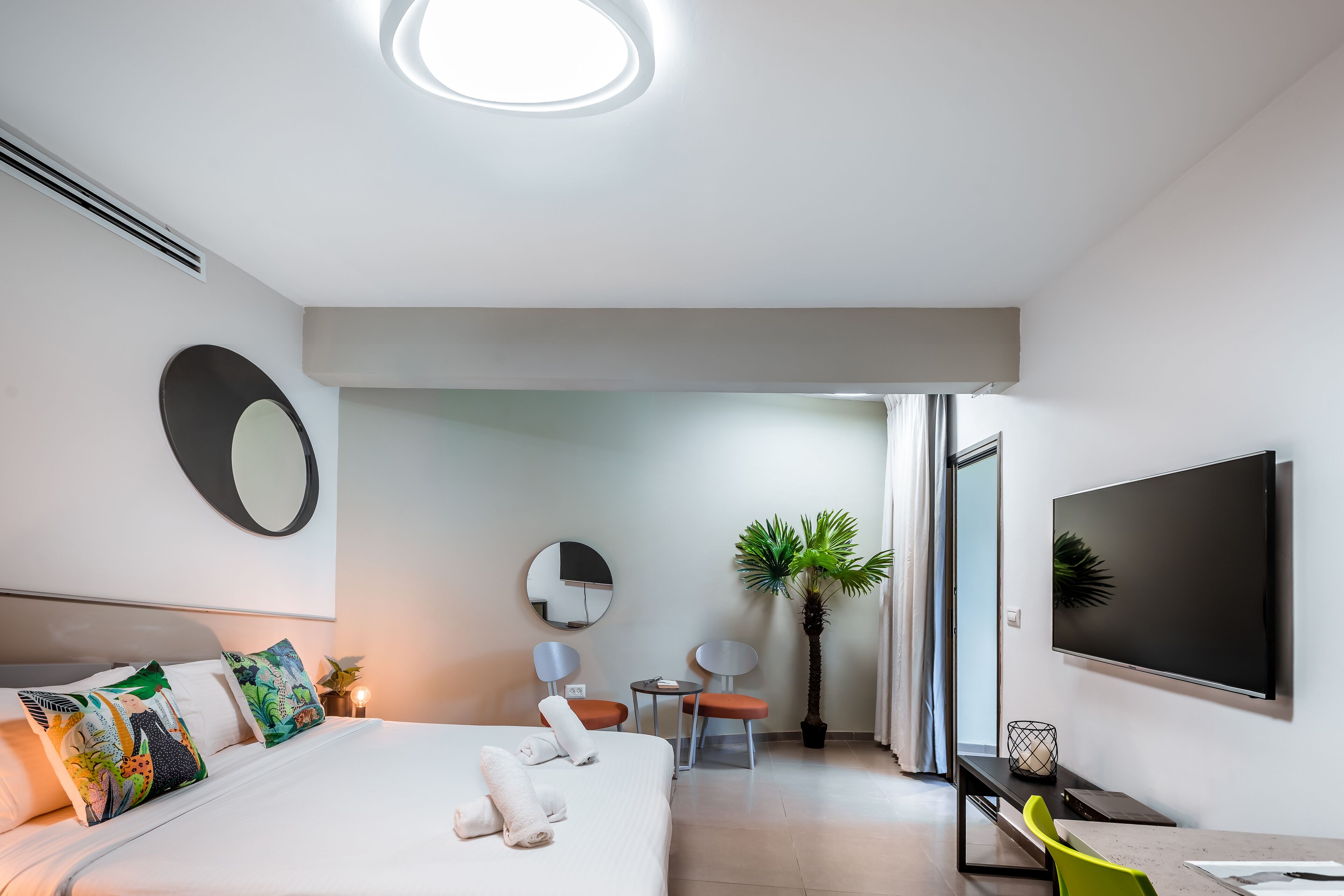 Una habitación de hotel moderna con una cama grande, un televisor de pantalla plana, un escritorio con una silla y una planta en maceta.