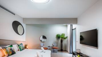 Una habitación de hotel moderna con una cama grande, un televisor de pantalla plana, un escritorio con una silla y una planta en maceta.