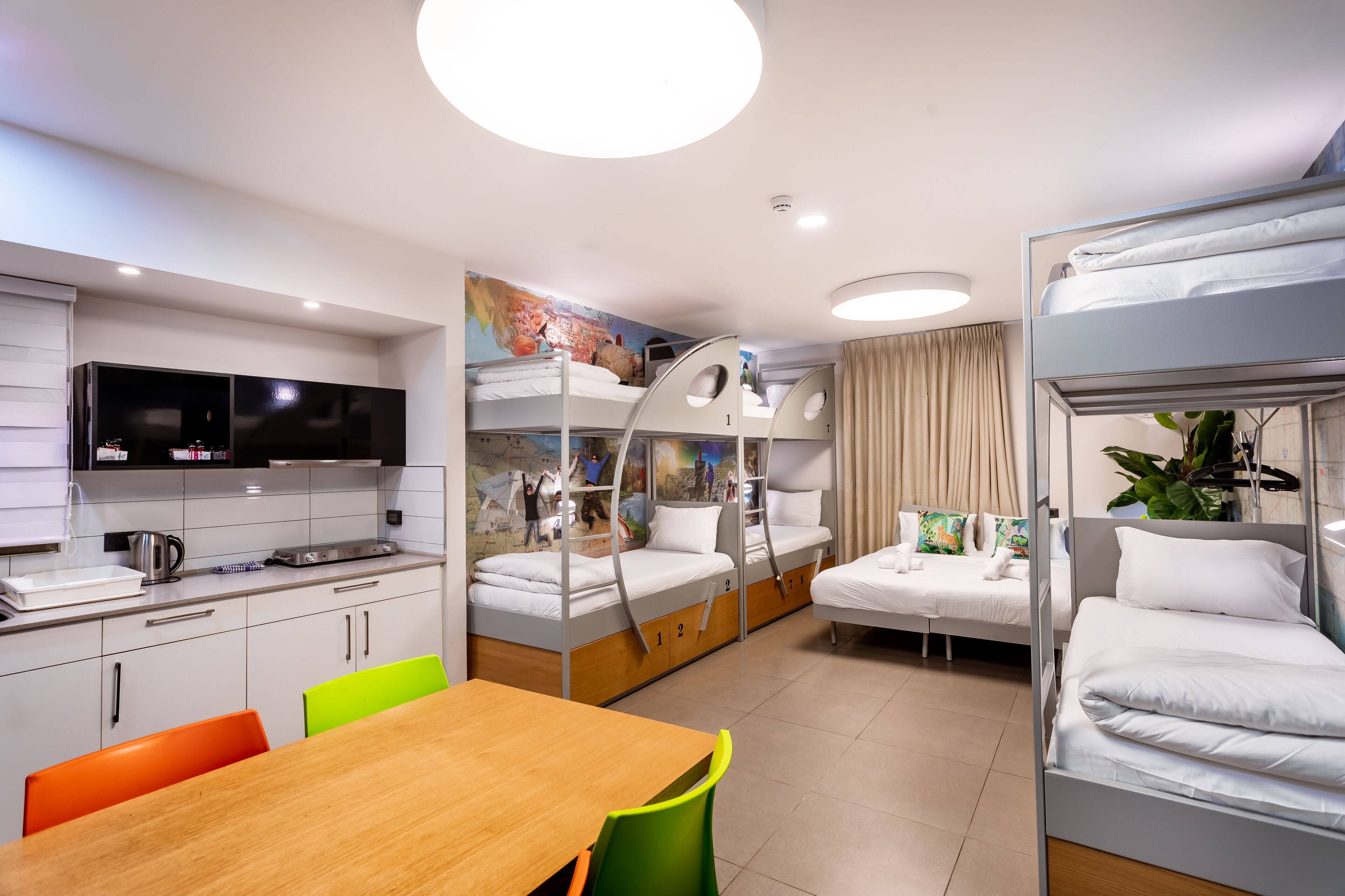 Een kleine hotelkamer met stapelbedden, een kitchenette, een eethoek en een televisie.