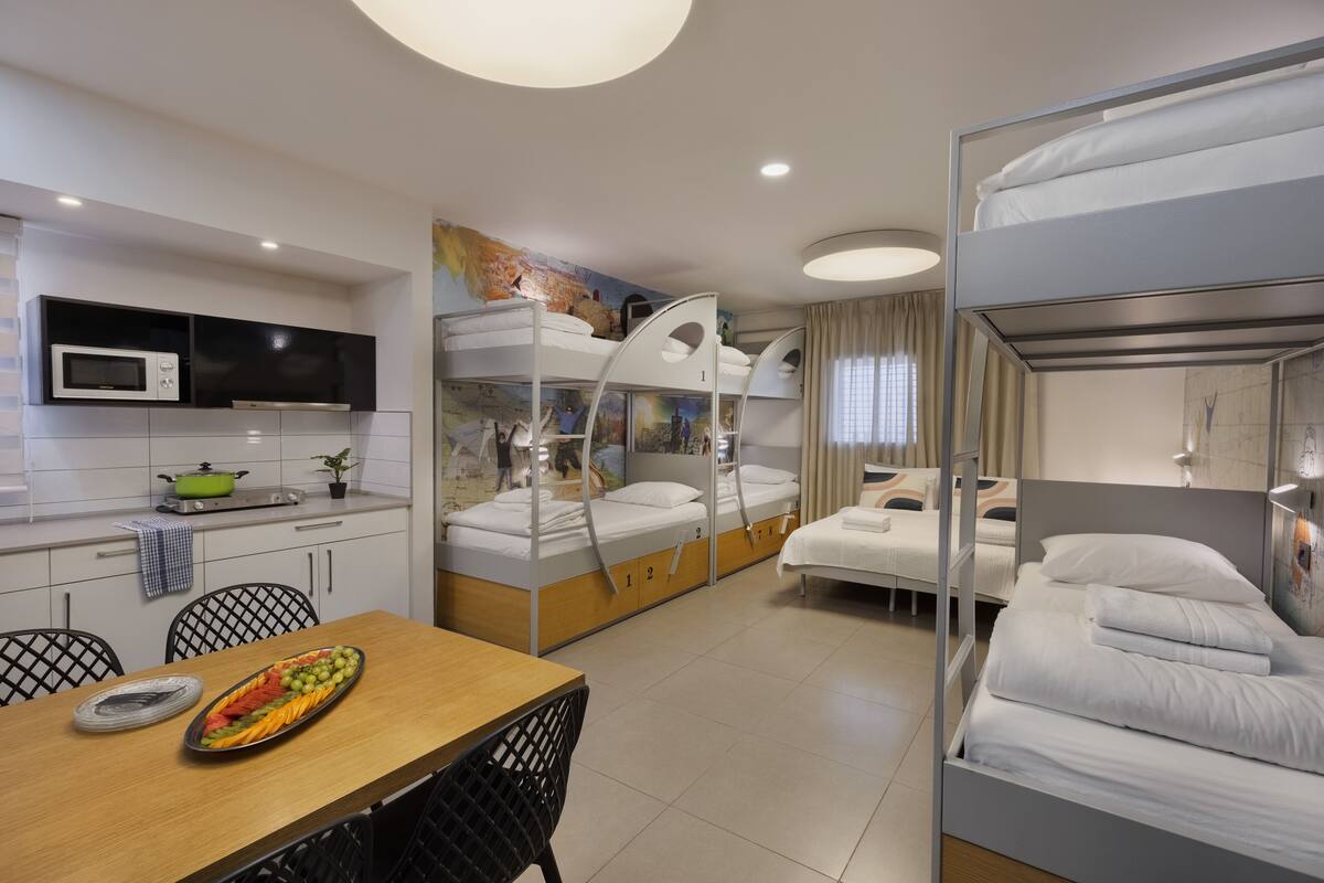 A compact hotel room with bunk beds, a kitchenette, a dining area, and a bathroom.