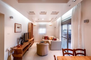 Una sala de estar moderna con sofá, reposapiés, mesa de centro de madera y televisor sobre un mueble de madera.