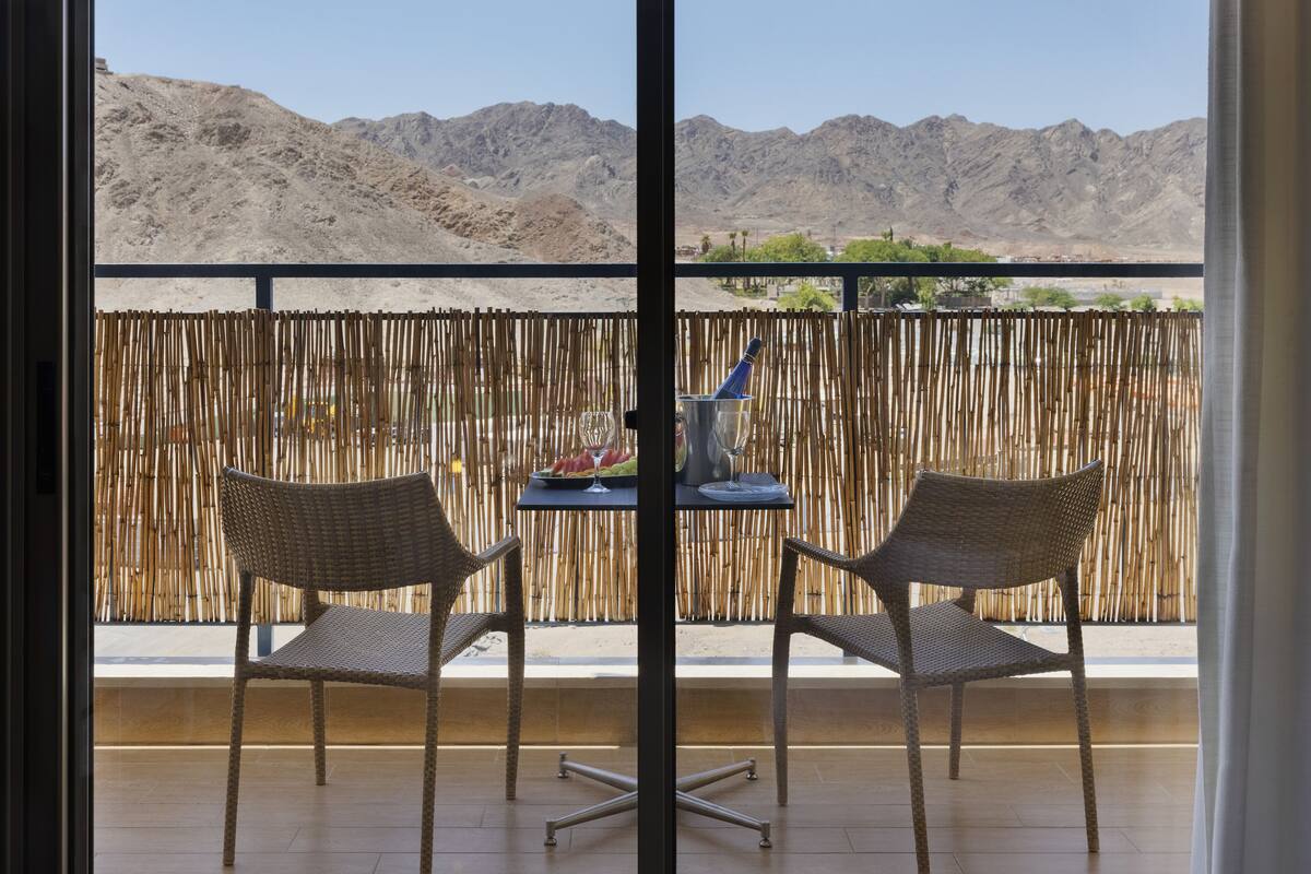 A balcony with wicker chairs and a table, a bamboo fence, and a view of mountains.