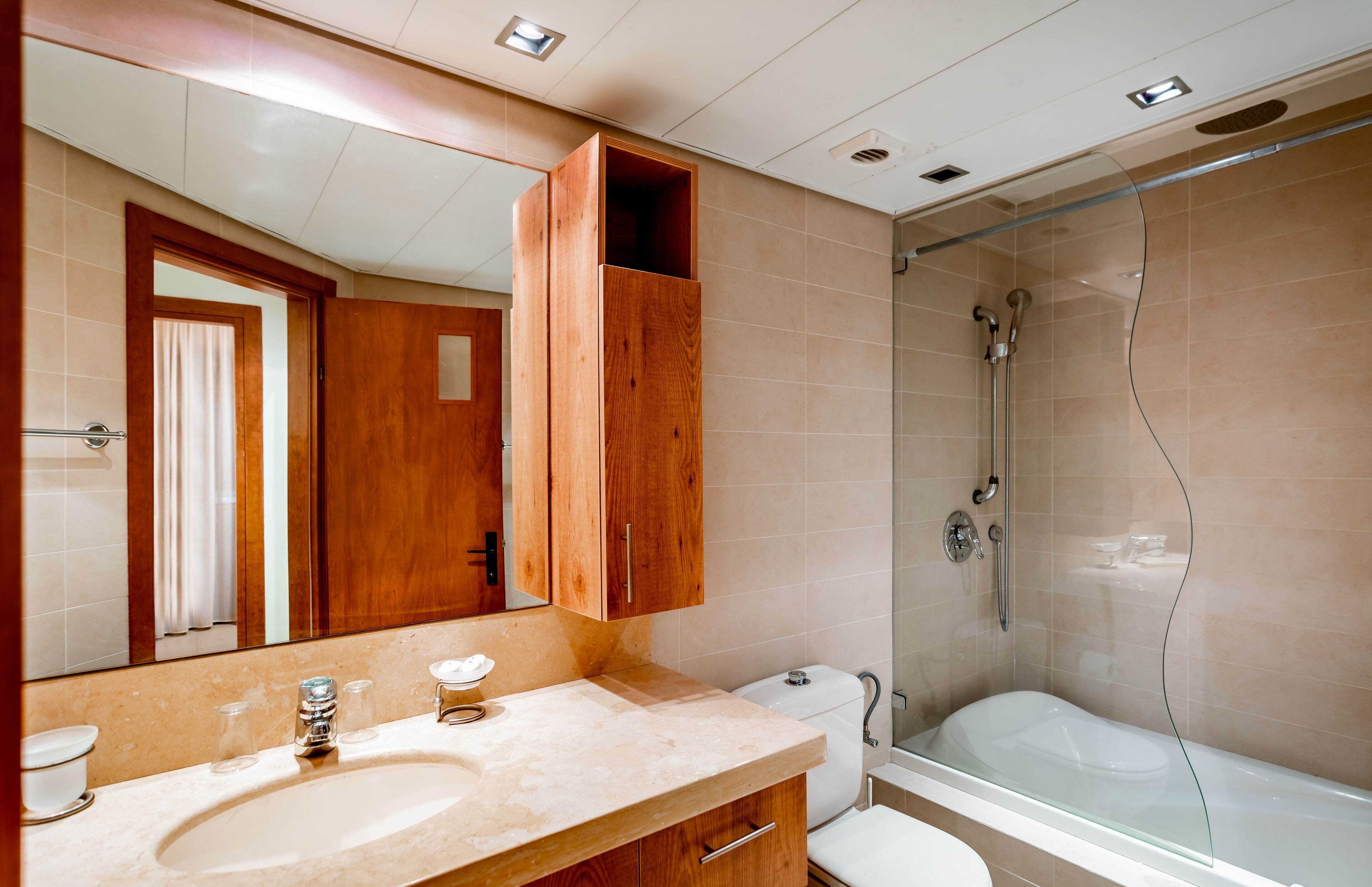 A modern bathroom with a large mirror, wooden vanity, a bathtub, and a glass shower enclosure.