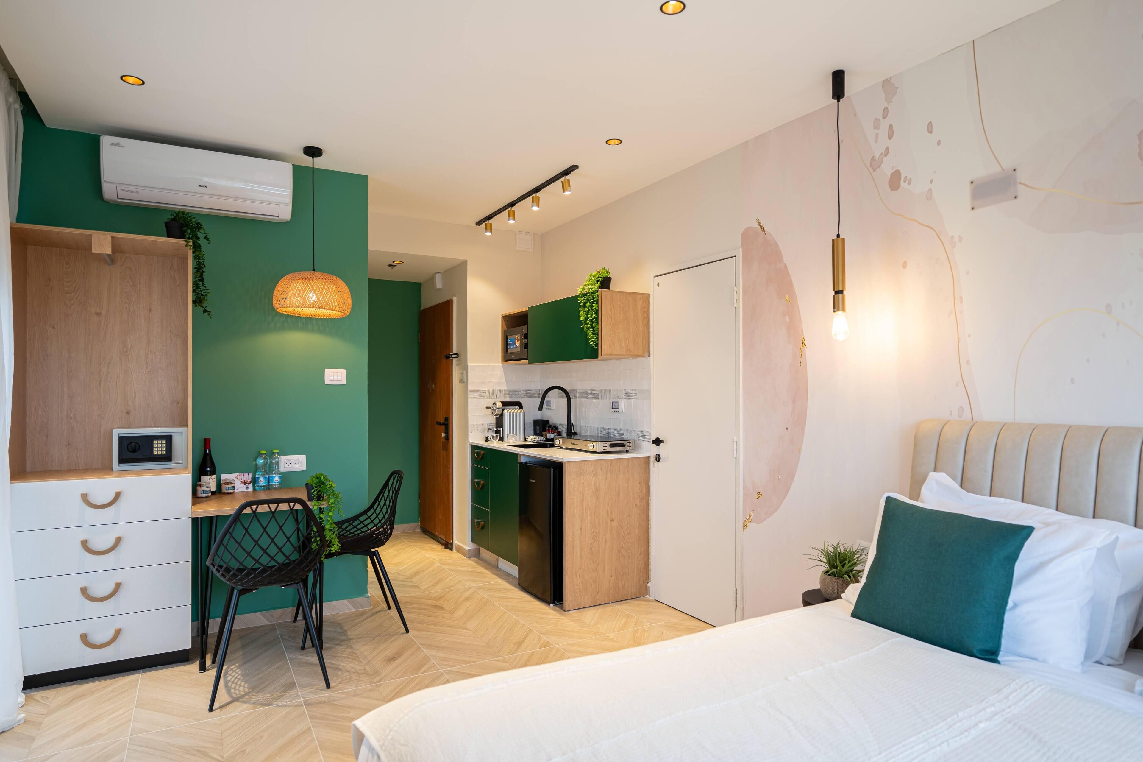 Ein kompaktes Hotelzimmer mit einem Bett, einem Schreibtisch mit Stuhl, einer Küchenzeile und einer grünen Wand.