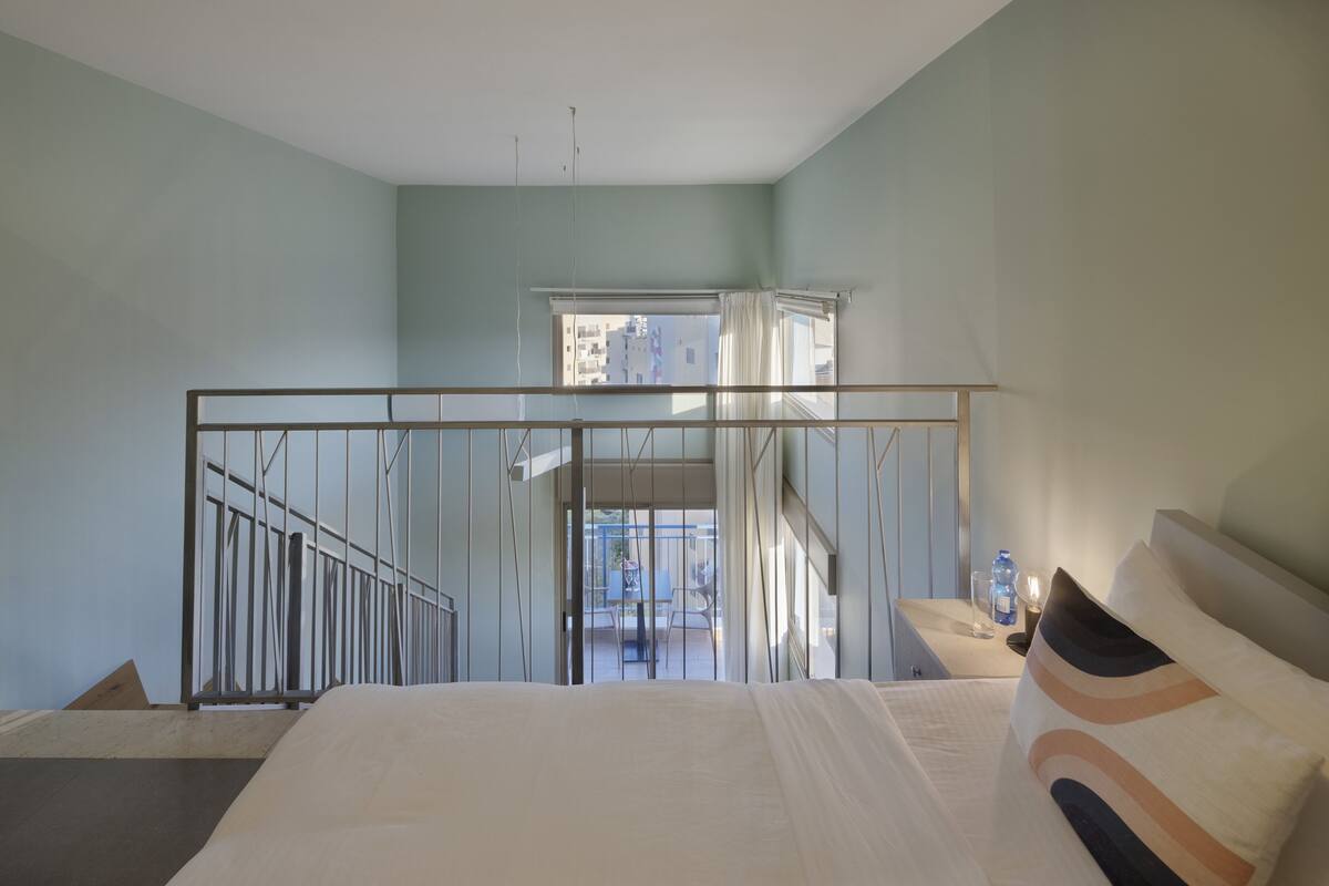 A bedroom with a bed, a nightstand, a window, and a view of the outside.