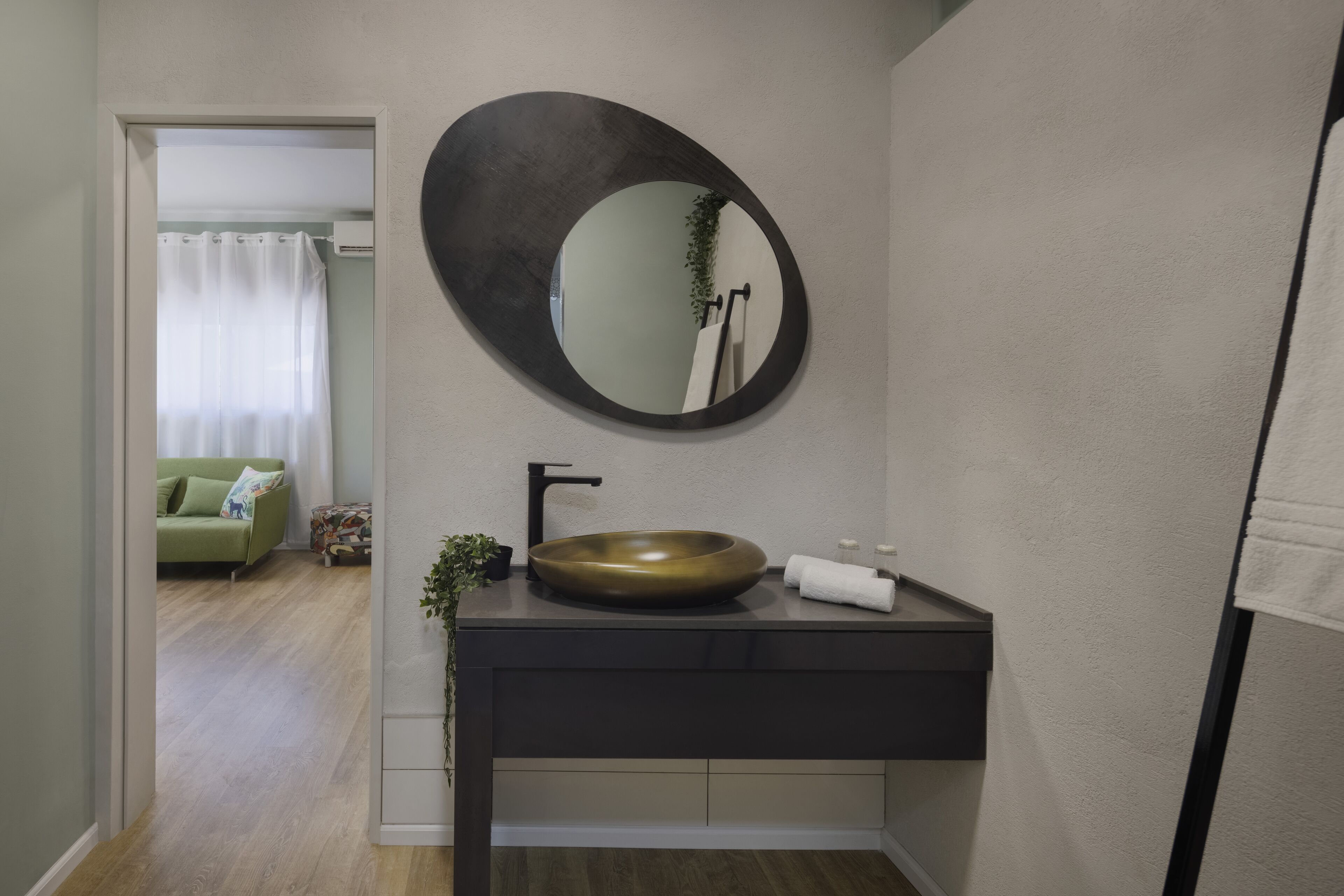 Un baño moderno con un espejo redondo, un lavamanos negro y un perchero para toallas.
