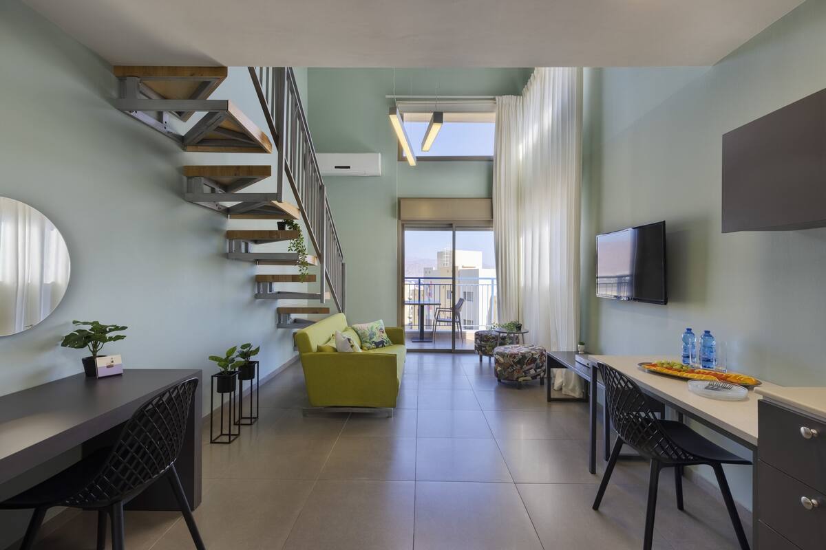A modern living space with a staircase, a sofa, a dining table, and a TV.