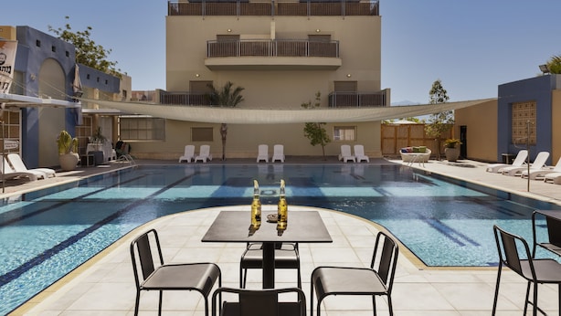 A swimming pool with lounge chairs and a table, surrounded by buildings with balconies. - Almog Eilat (Eilat)