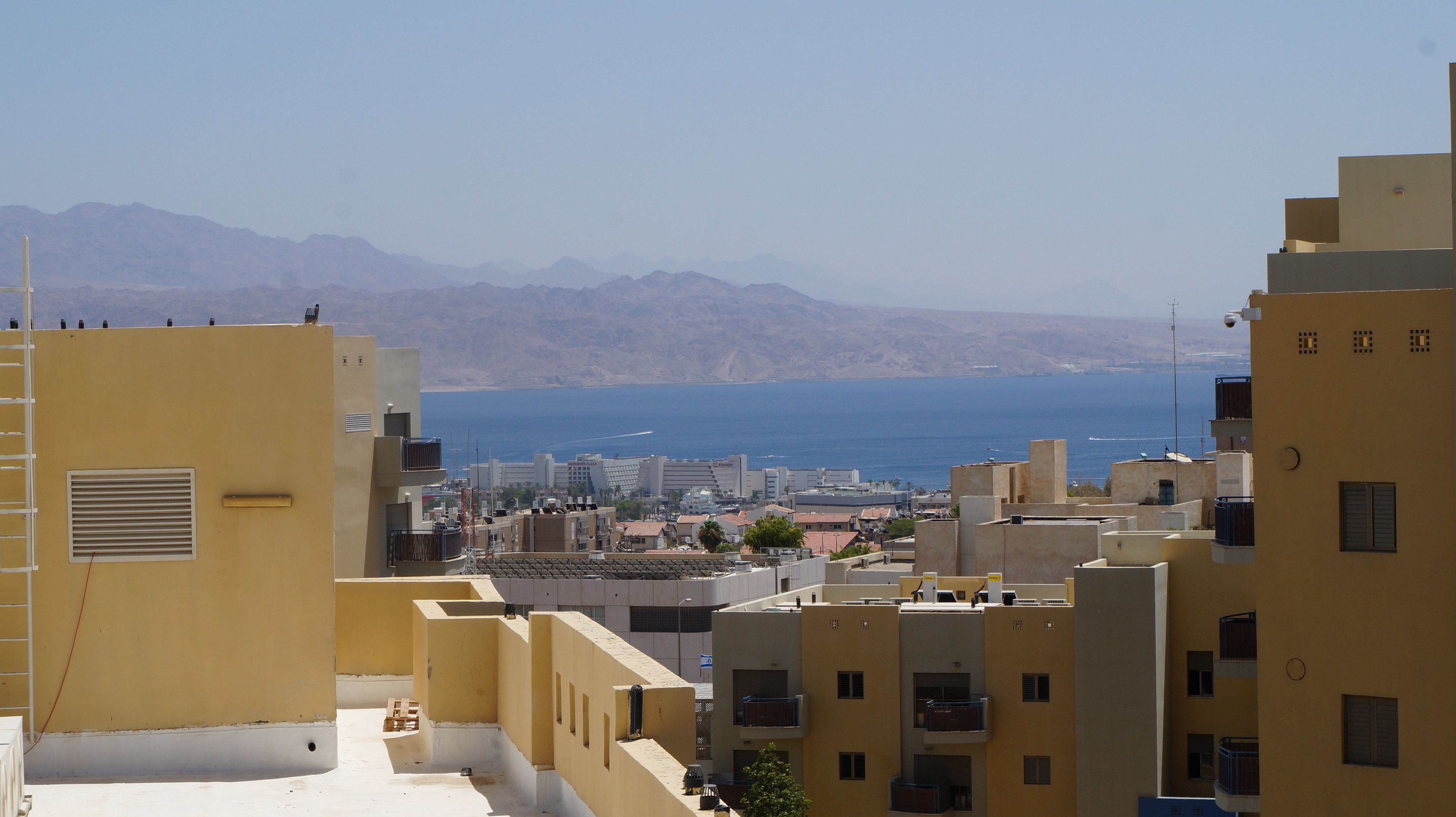 A coastal cityscape with yellow buildings, a view of the sea, and distant mountains.