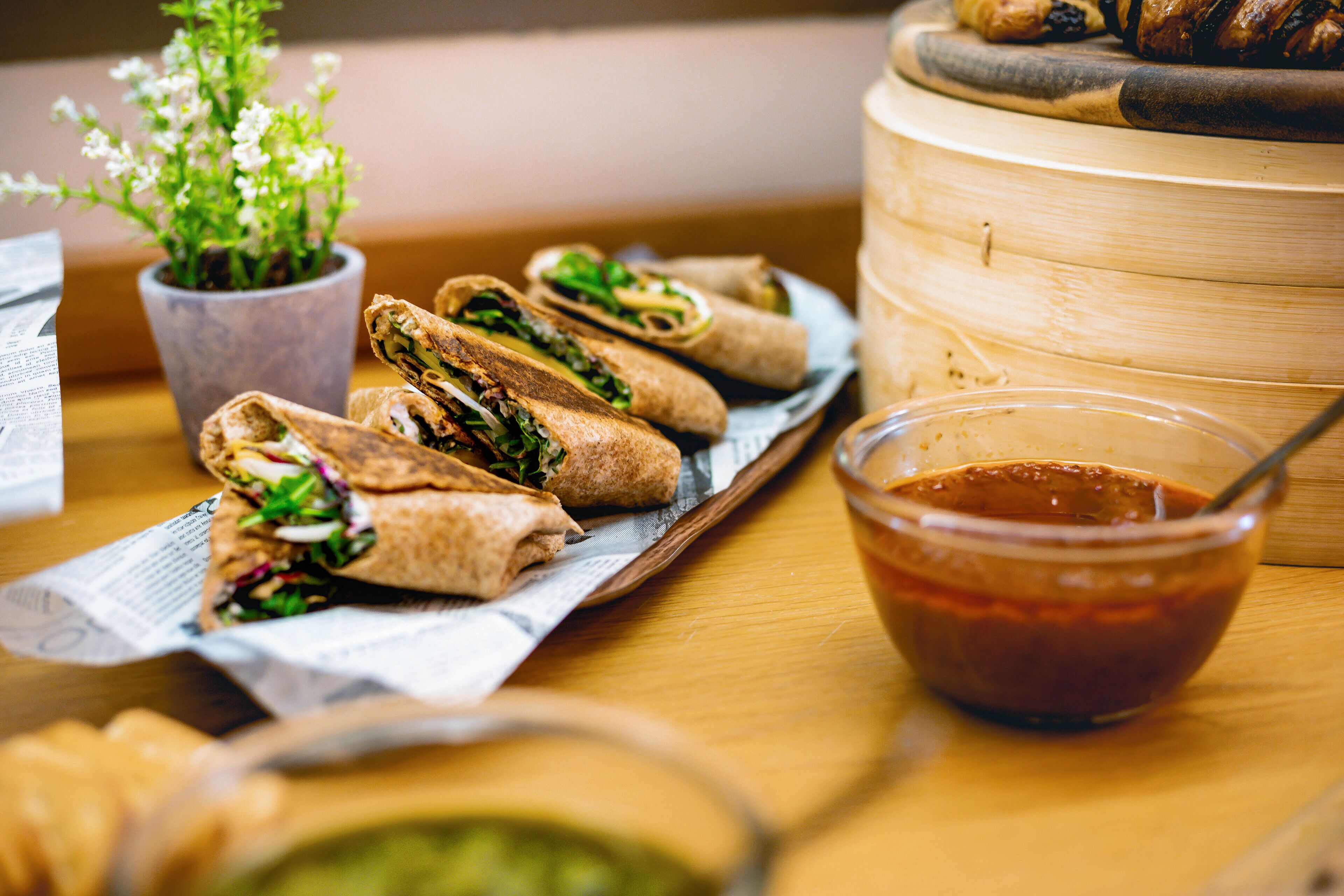 A wooden table with a tray of sandwiches, a bowl of sauce, and a potted plant.