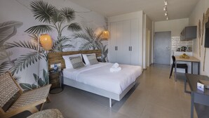 A modern hotel room with a large bed, a seating area with a chair, a small table, and a wall with a tropical leaf mural. - Almog Eilat (Eilat)