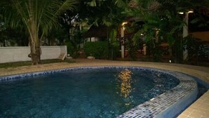 Una piscina con bordes de azulejos, rodeada de palmeras y plantas tropicales.