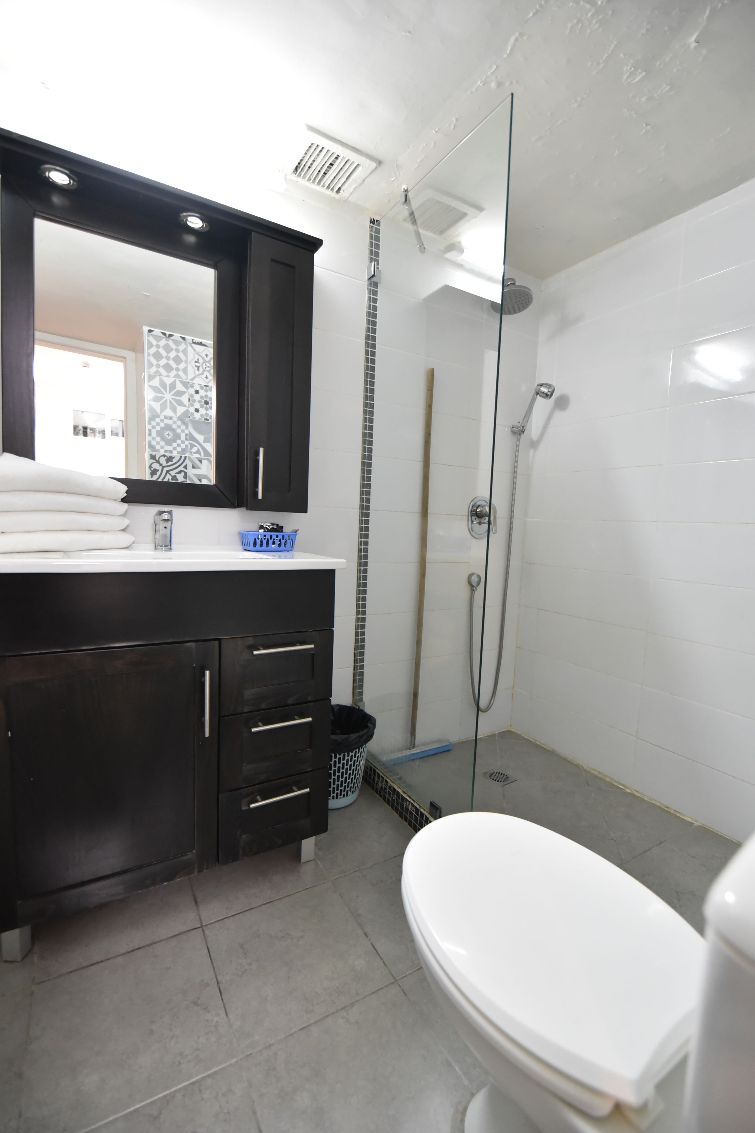 A bathroom with a white toilet, a dark wooden vanity with drawers, a mirror, and a shower area with a glass door.