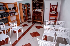 Ein Zimmer mit weißen Stühlen, einem Holzregal und einer Gebetsbank.
