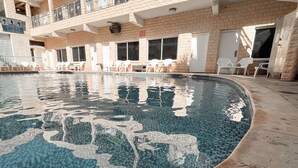 A swimming pool with a tiled pattern, surrounded by a brick building with multiple windows and a balcony. - Maman Hotel (Eilat)