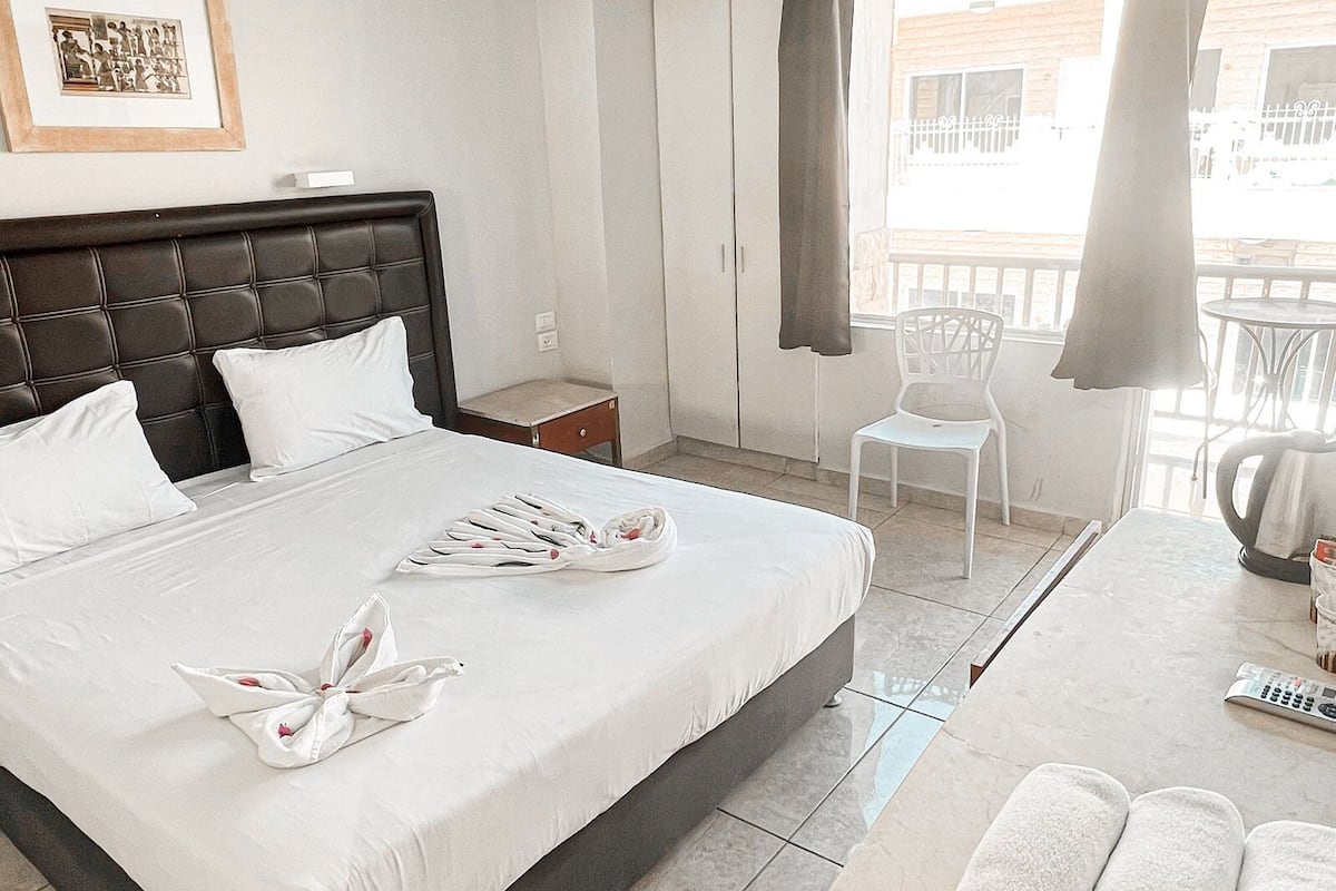 A hotel room with a large bed, a chair, a table, and a balcony with a view.