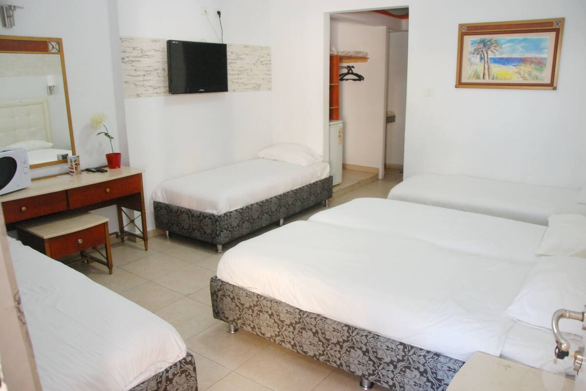A hotel room with three beds, a desk with a chair, a television mounted on the wall, and a painting on the wall.