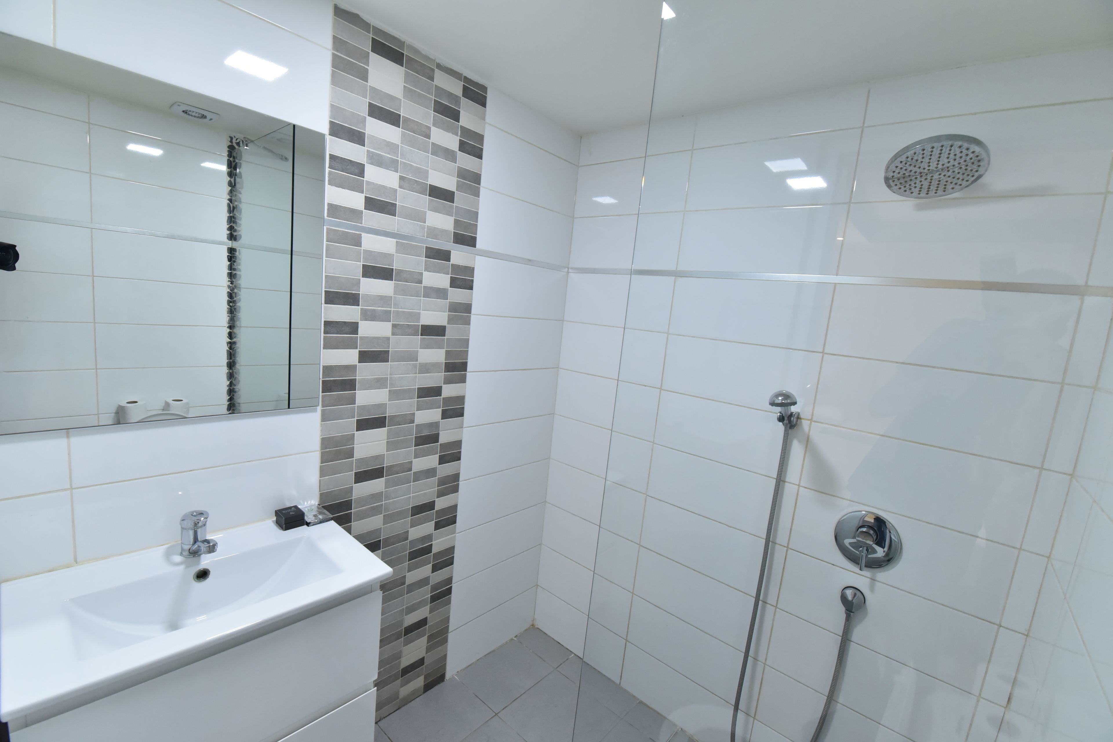 Ein modernes Badezimmer mit einem weißen Waschbecken, einem Spiegel und einer Dusche mit Duschbrause.