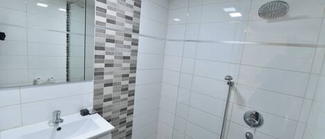 Une salle de bain moderne avec un lavabo blanc, un miroir et une douche équipée d’un pommeau de douche à main.