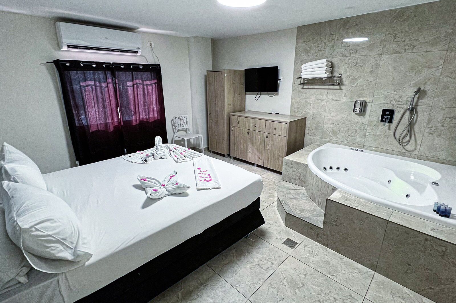 Una habitación de hotel con cama, baño con bañera, televisión y minibar.