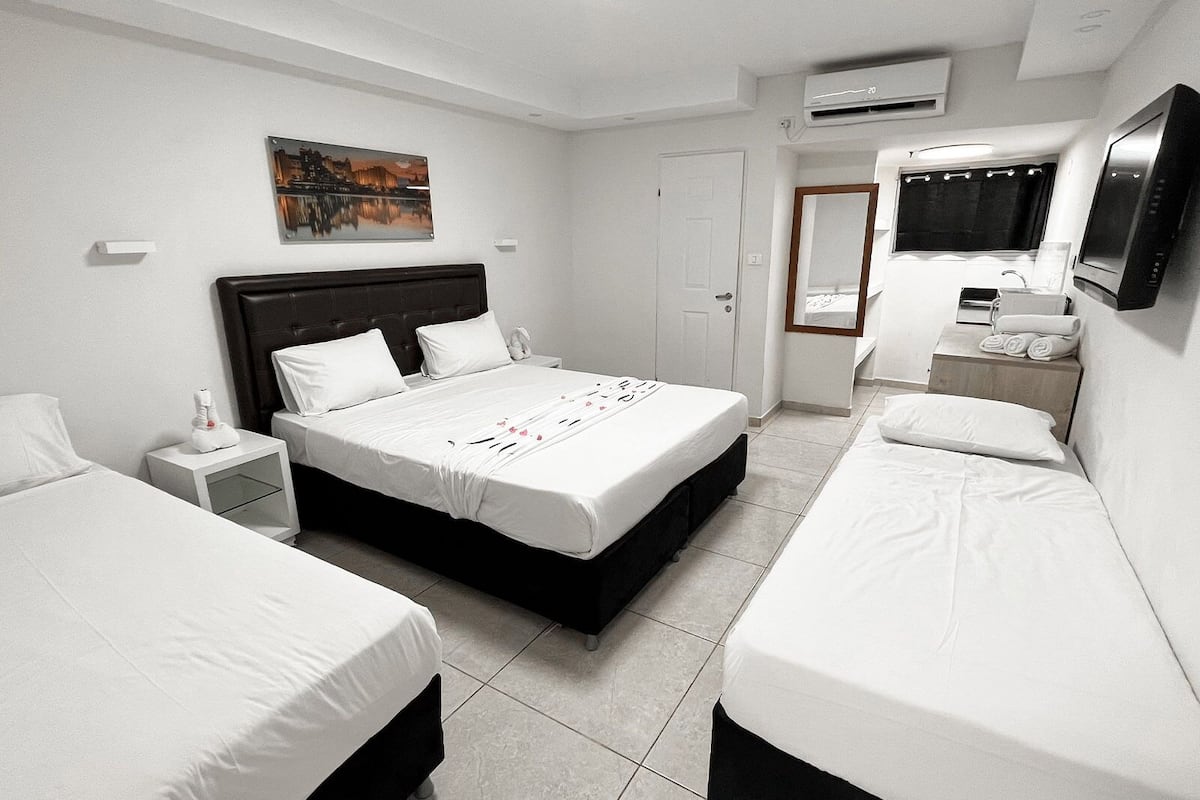 A hotel room with a large bed, two bedside tables, a TV, and an air conditioning unit.