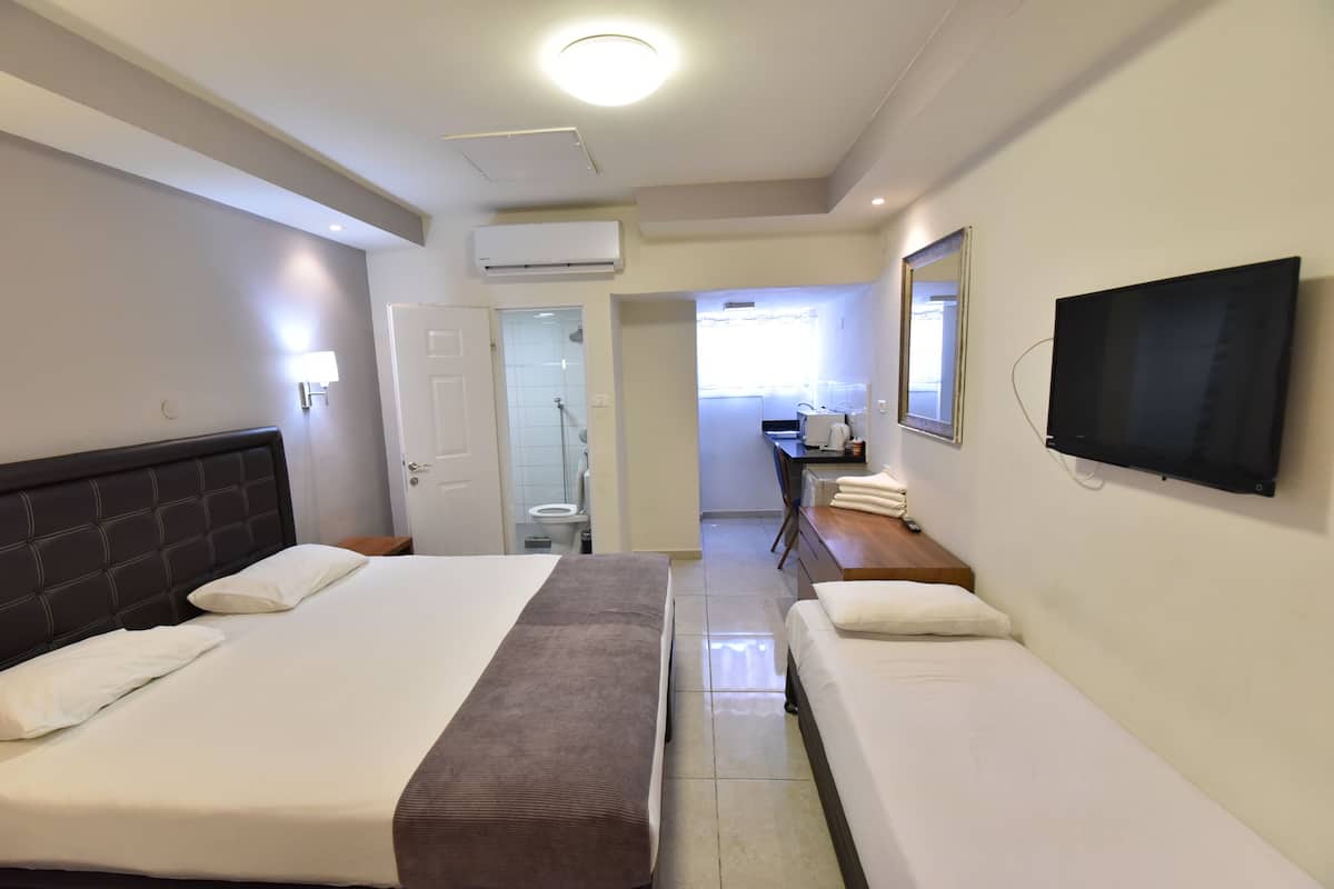 A hotel room with a large bed, a smaller bed, a TV, a desk, and a bathroom visible through an open door.