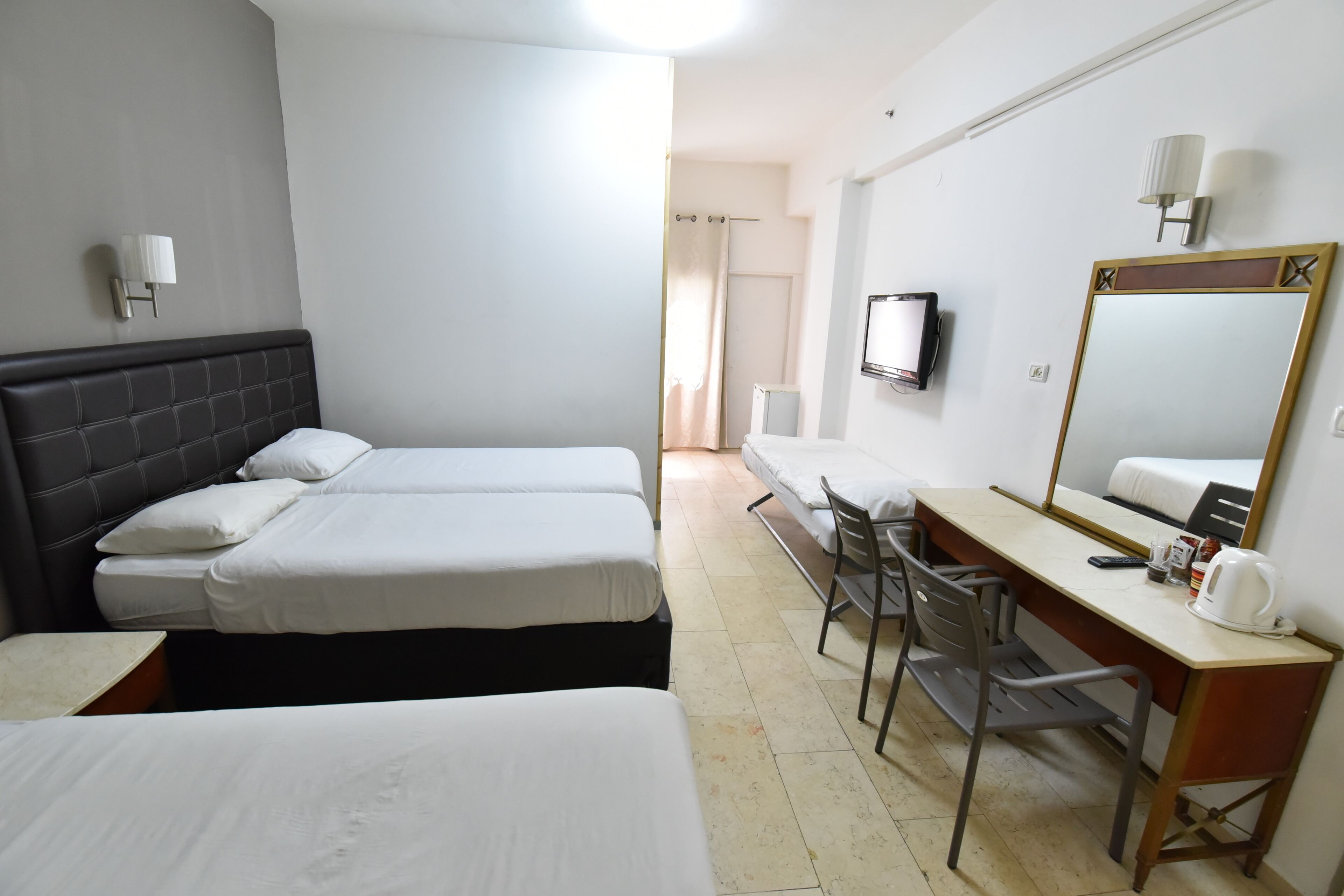 A hotel room with two single beds, a desk with a chair, a television, and a large mirror.