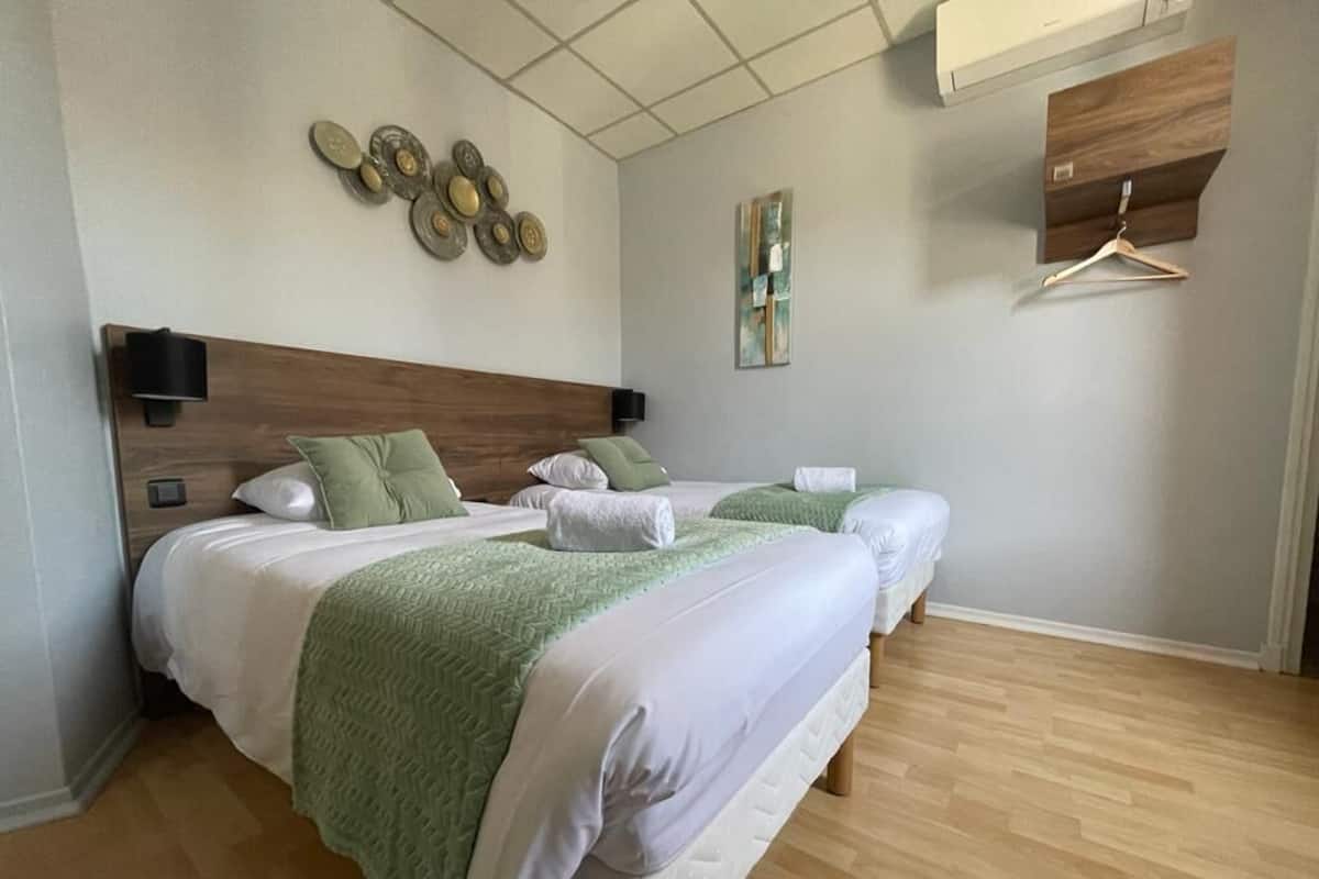 A hotel room with two beds, a wooden headboard, a wall-mounted air conditioner, and a wooden floor.