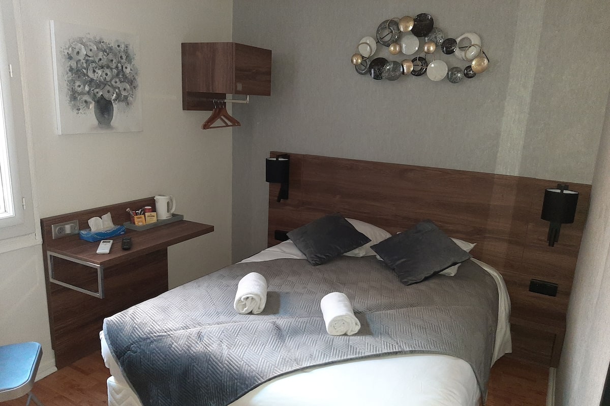 A neatly arranged hotel room with a bed, bedside table, and a small desk with a chair.