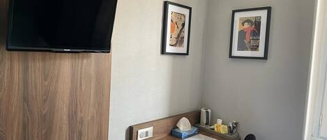 Habitación de hotel con un escritorio de madera, un televisor de pantalla plana en la pared y dos cuadros enmarcados.