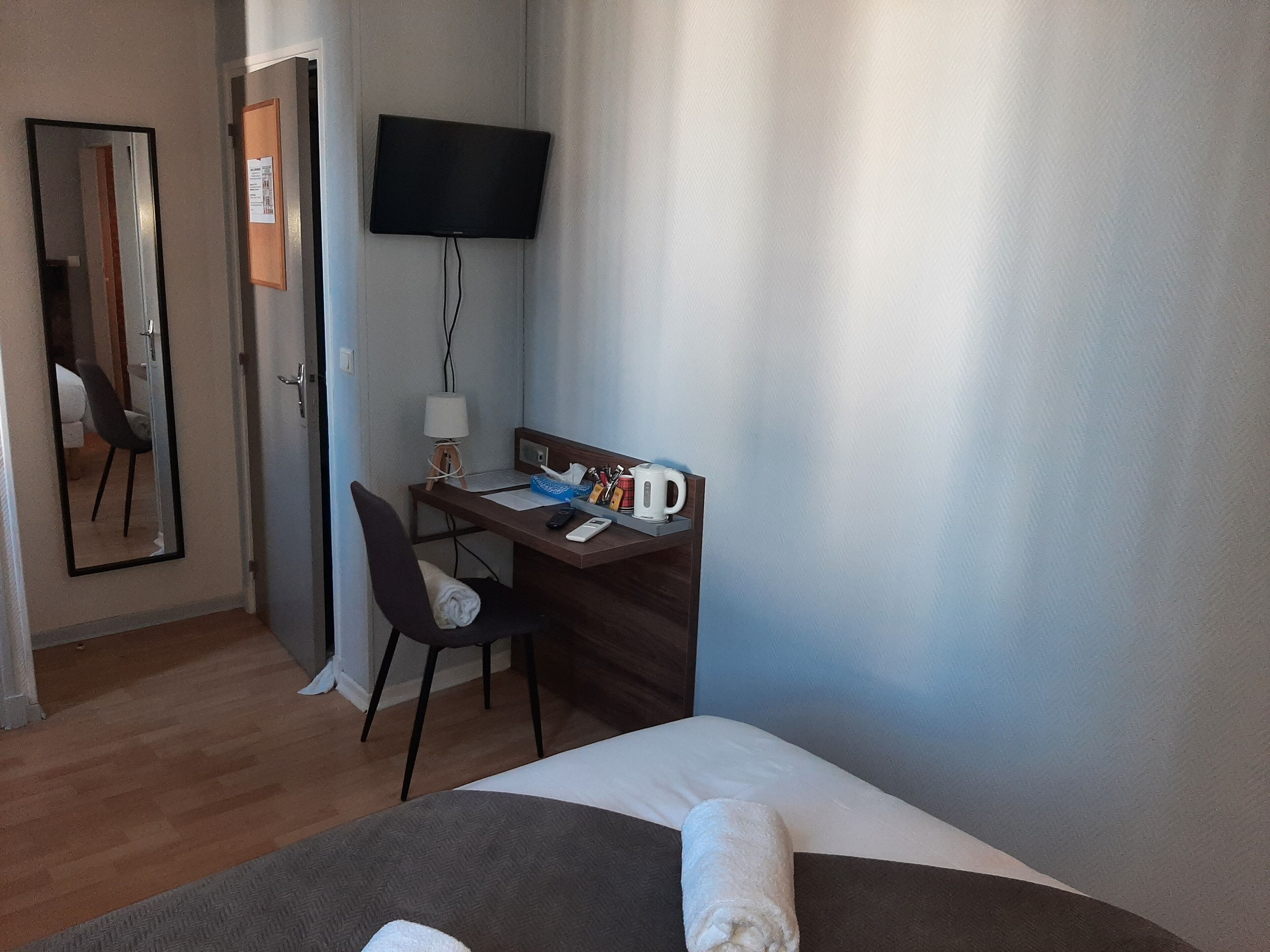 Hotelkamer met een bed, een bureau met stoel, een aan de muur bevestigde televisie en een raam met gordijnen.