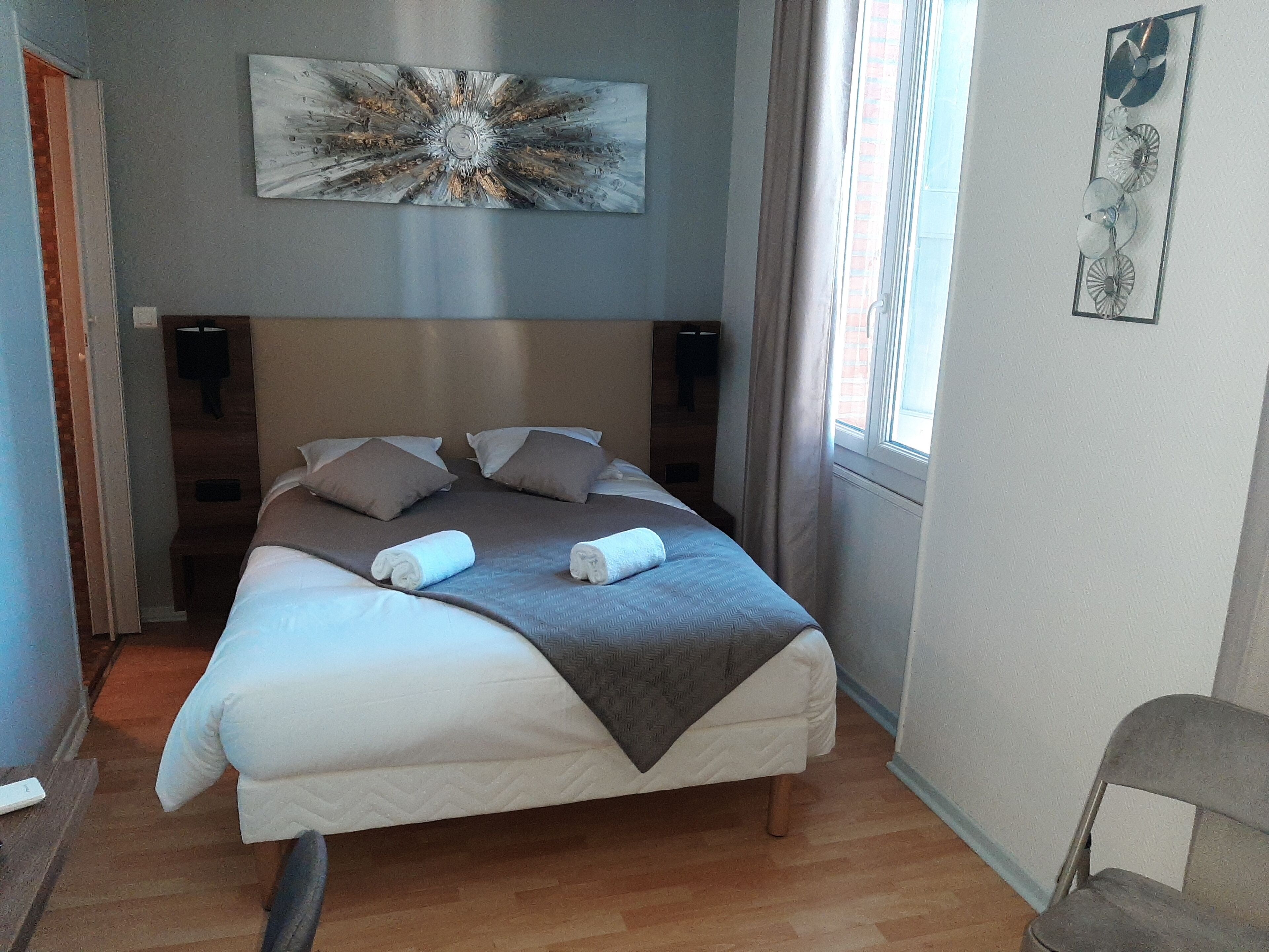 A neatly made bed with pillows and a blanket, a wall art piece above it, and a window with curtains.