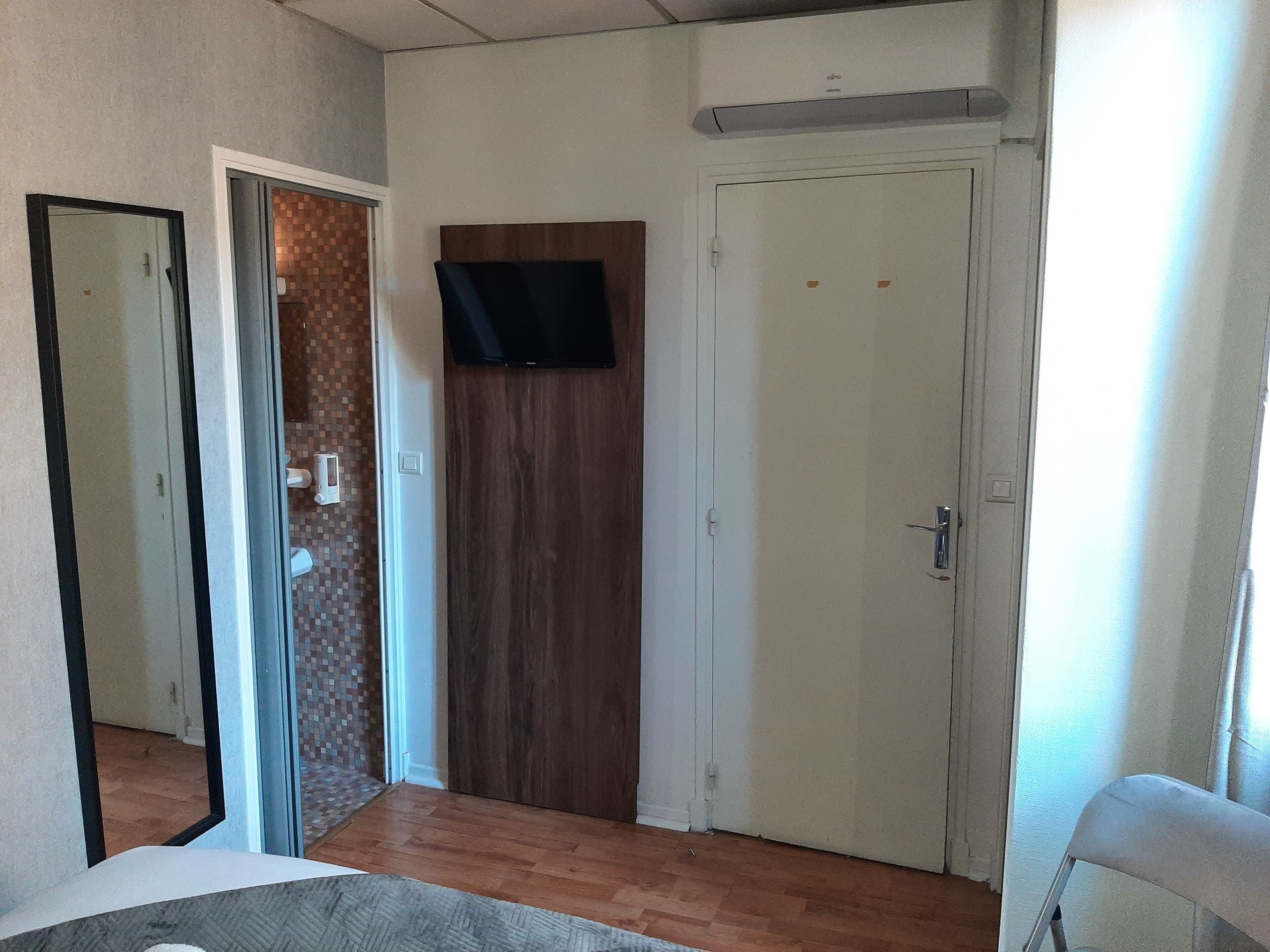Una habitación con una puerta de madera, una puerta blanca y un espejo en la pared izquierda.