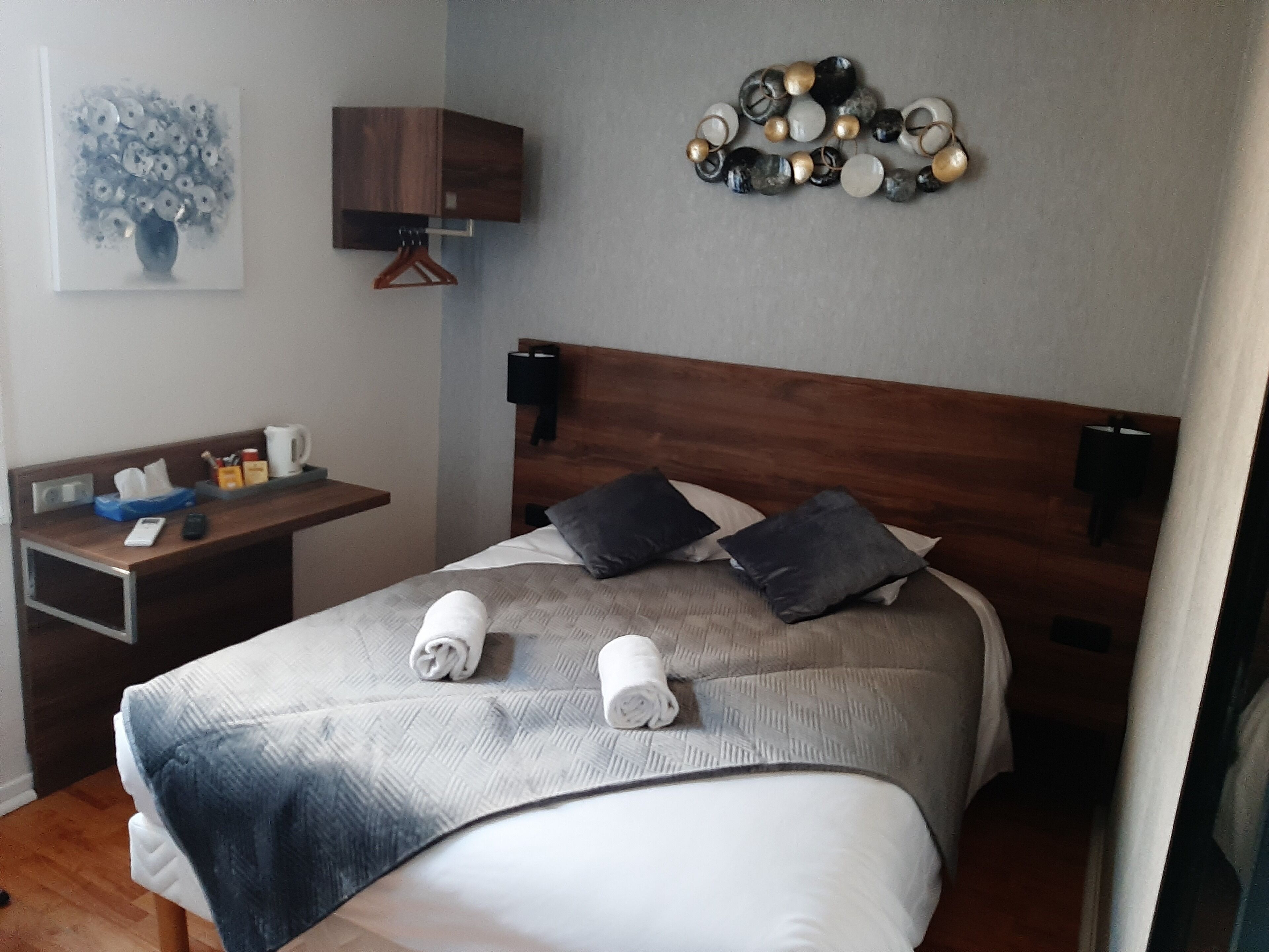 Habitación de hotel ordenada con cabecera de madera, una mesita de noche con lámpara, un cuadro en la pared y un elemento decorativo sobre la cama.