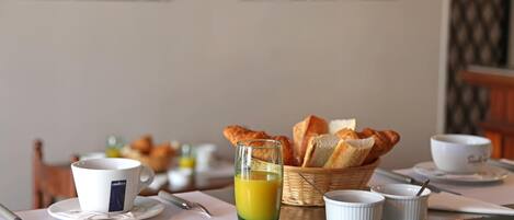 Un desayuno con una taza, vaso de jugo de naranja, pan y recipientes pequeños sobre una mesa.