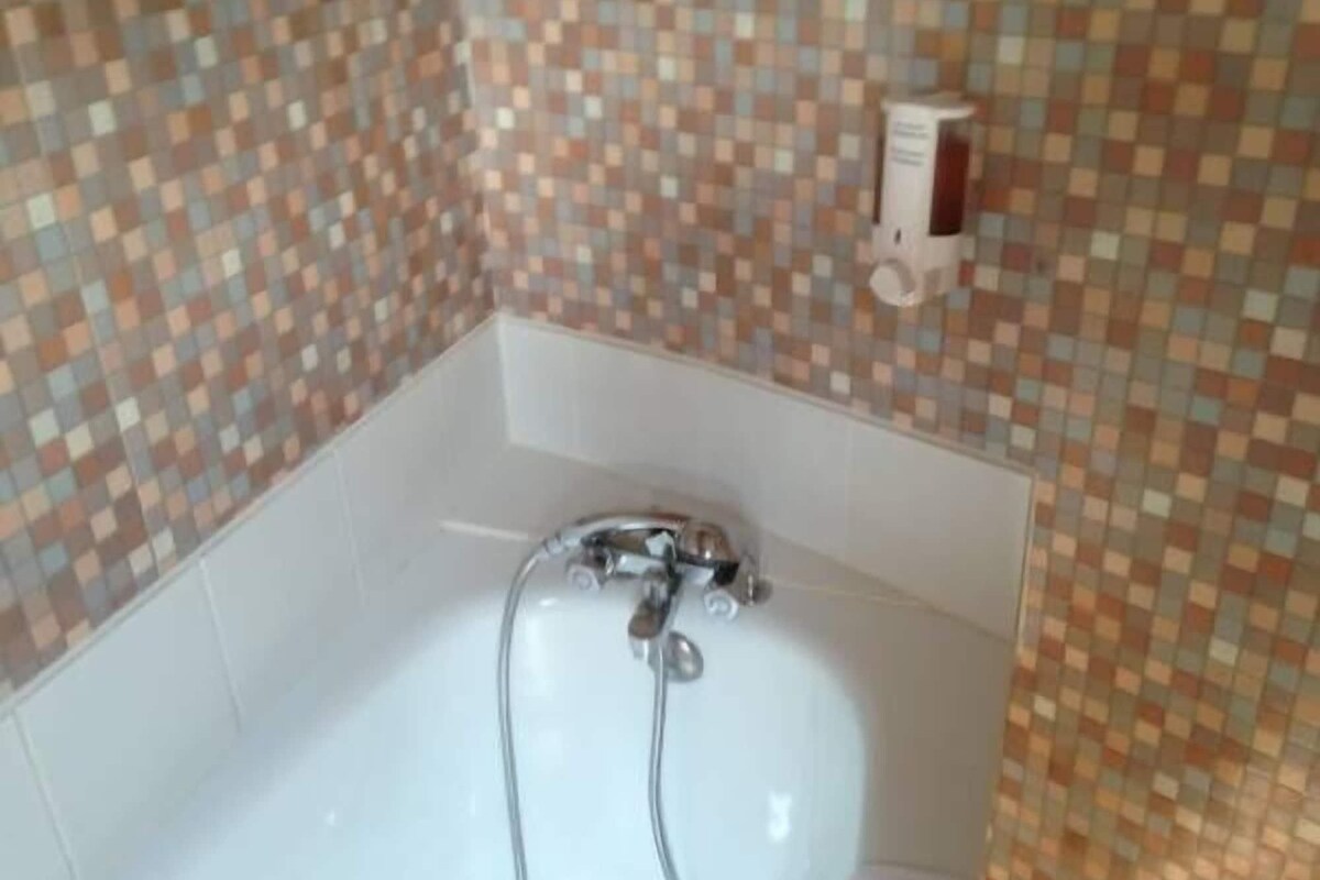 A bathtub with a showerhead, tiled walls, and a soap dispenser.