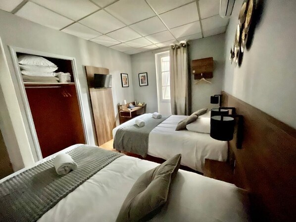 Una habitación de hotel con dos camas, un armario, un escritorio y una ventana con cortinas.