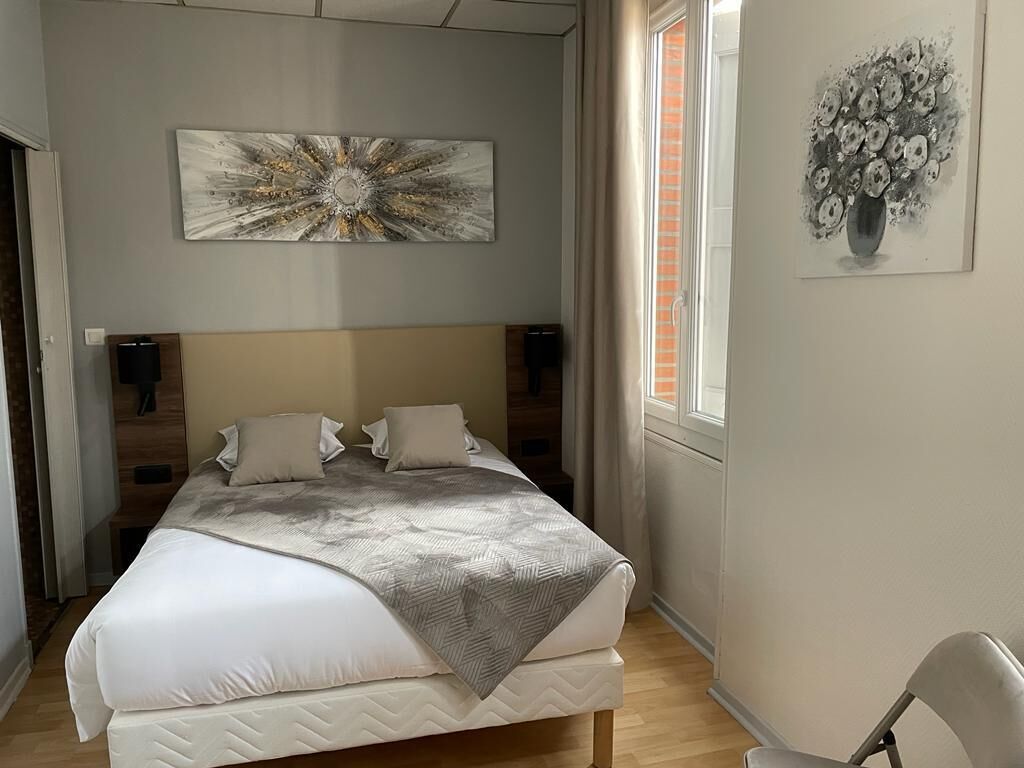A bedroom with a bed, a headboard, a wall-mounted artwork, a window with curtains, and a chair.