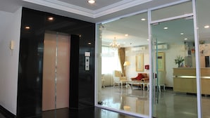 A modern hotel lobby with a glass partition, a reception desk, a chandelier, and a seating area with a red sofa. - Romance Hotel Srinakarin (Bangkok)