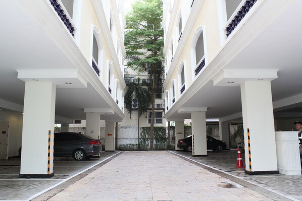 A covered parking area with multiple cars, white pillars, and a central tree.