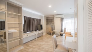 A modern, well-lit room with a wooden floor, a TV, a desk, a chair, and a small table. - Romance Hotel Srinakarin (Bangkok)