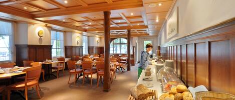 A spacious dining area with wooden paneling, multiple tables and chairs, and a buffet line with various food items.