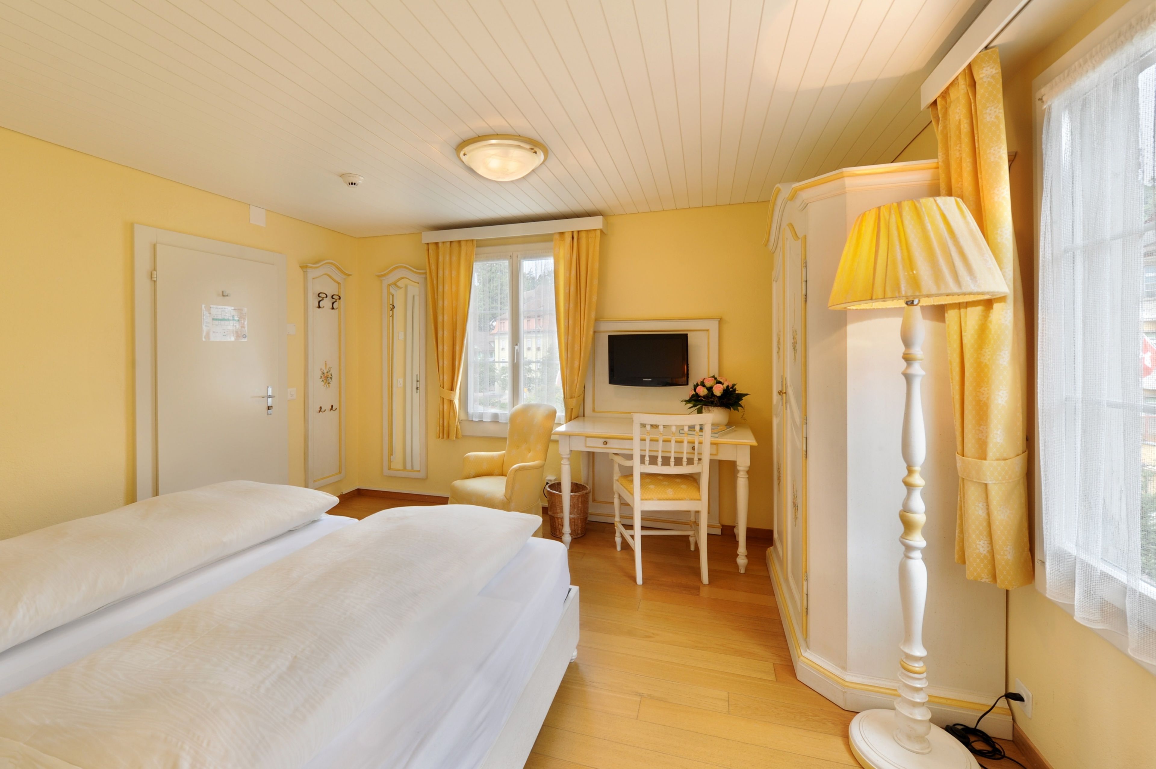 A hotel room with two beds, a desk with a TV, a lamp, and a window with curtains.
