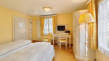 A hotel room with two beds, a desk with a TV, a lamp, and a window with curtains.