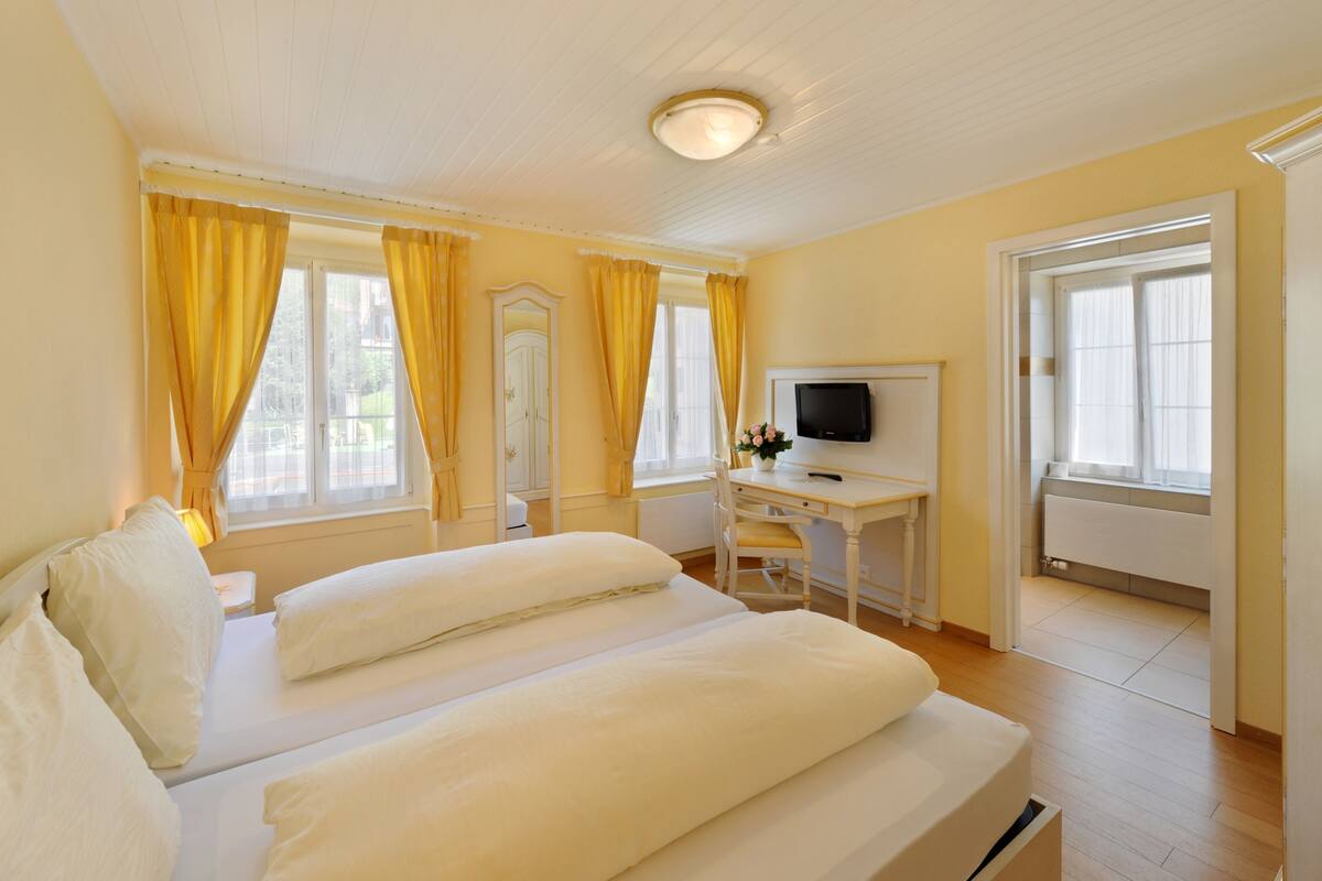 Une chambre d’hôtel avec un lit, un bureau avec une télévision et une fenêtre avec des rideaux.