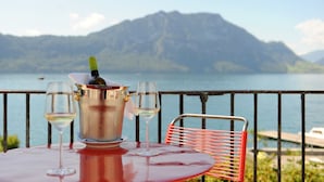 Una mesa con un balde de vino y copas, una silla roja, y una vista panorámica de un lago y montañas.